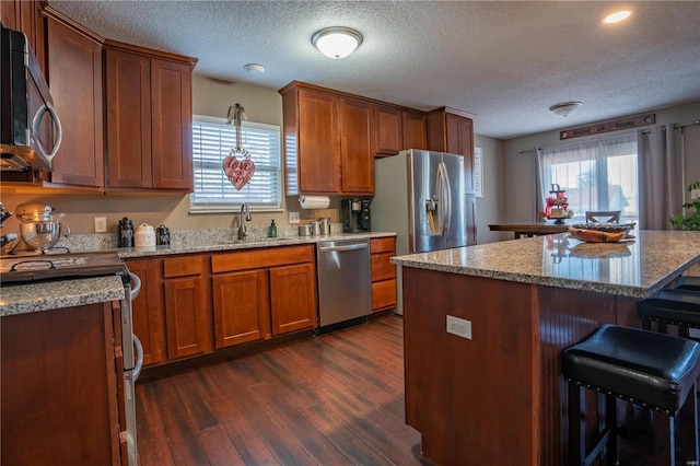 kitchen with dark wood-type flooring, sink, a kitchen breakfast bar, a kitchen island, and stainless steel appliances