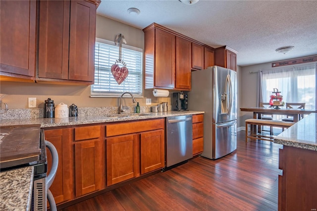 kitchen featuring sink, dark wood-type flooring, stainless steel appliances, light stone counters, and a textured ceiling