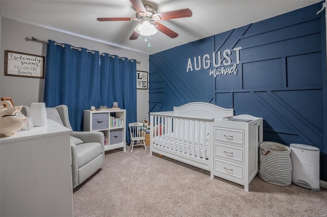 bedroom with ceiling fan, light colored carpet, a nursery area, and a textured ceiling