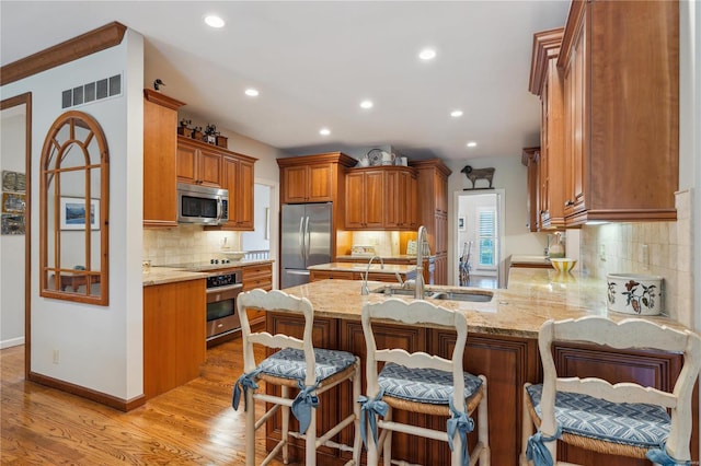 kitchen with a kitchen bar, sink, appliances with stainless steel finishes, kitchen peninsula, and light stone countertops