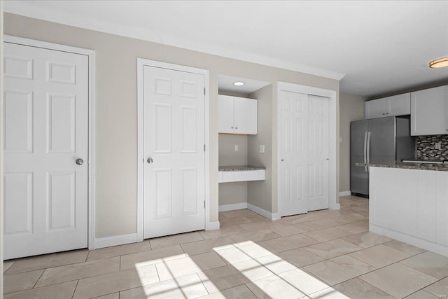 kitchen featuring white cabinetry, dark stone counters, decorative backsplash, and stainless steel refrigerator