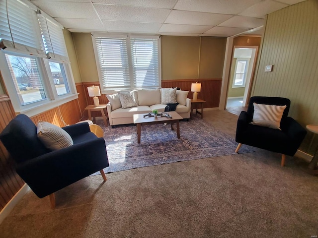 living area featuring a wainscoted wall, carpet floors, wood walls, and a drop ceiling