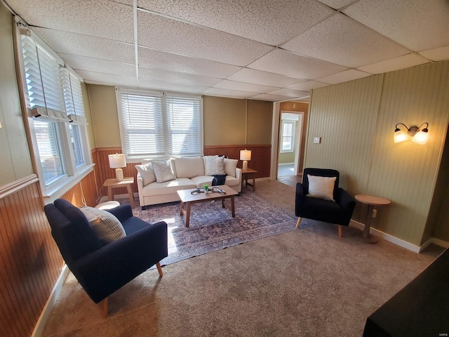 carpeted living room with wooden walls and a drop ceiling