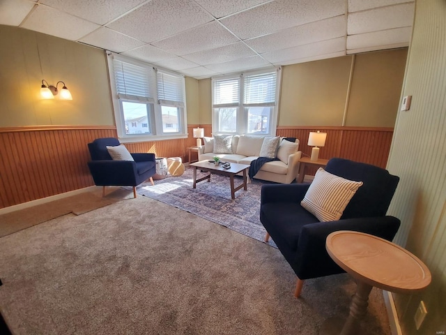 carpeted living room with a wainscoted wall, a drop ceiling, and wooden walls