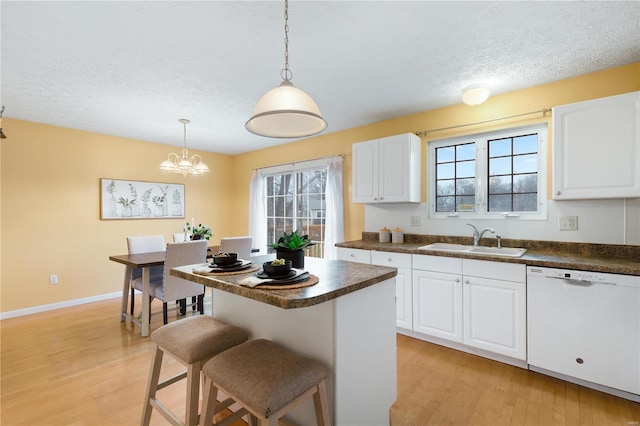 kitchen with sink, a breakfast bar, dishwasher, white cabinetry, and hanging light fixtures