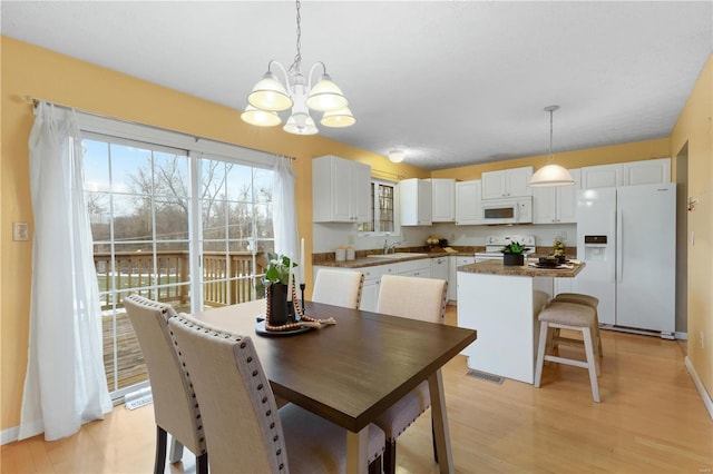 dining space with an inviting chandelier, sink, and light hardwood / wood-style floors