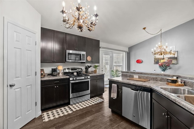 kitchen with dark wood-type flooring, lofted ceiling, an inviting chandelier, hanging light fixtures, and appliances with stainless steel finishes