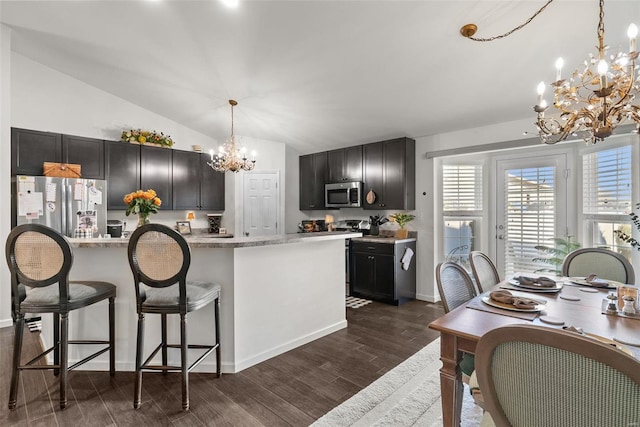 kitchen with hanging light fixtures, stainless steel appliances, light stone countertops, a center island with sink, and a chandelier