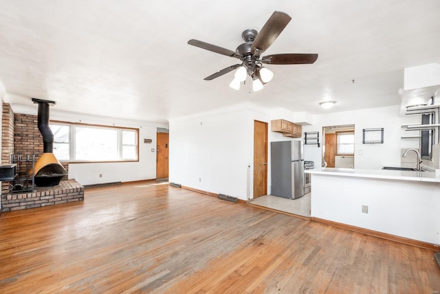 unfurnished living room featuring ceiling fan, sink, light hardwood / wood-style flooring, and a wood stove