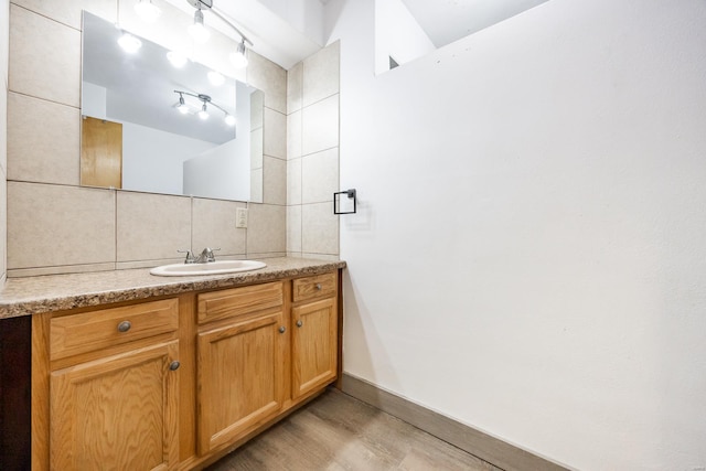 bathroom featuring hardwood / wood-style flooring, rail lighting, tile walls, tasteful backsplash, and vanity