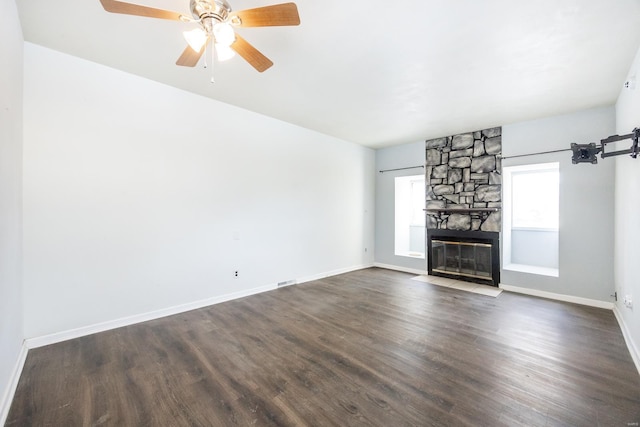 unfurnished living room featuring dark hardwood / wood-style flooring, a stone fireplace, and ceiling fan