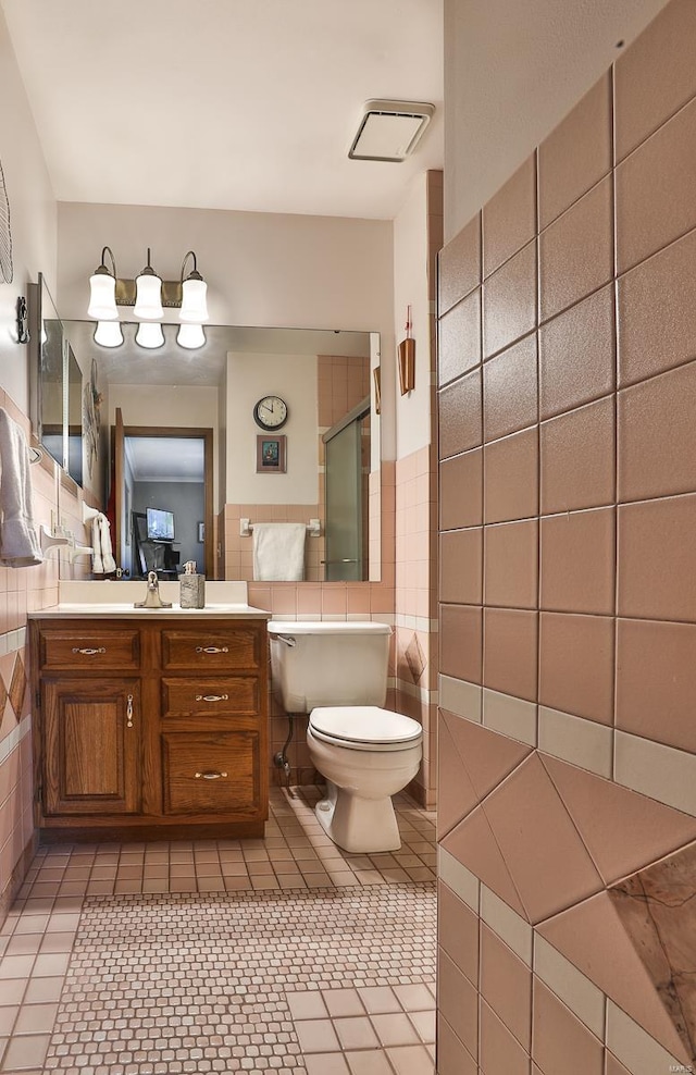 bathroom featuring toilet, a shower with shower door, tile walls, vanity, and tile patterned flooring