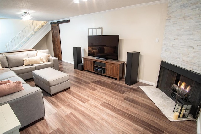 living room featuring a fireplace, ornamental molding, a barn door, and light hardwood / wood-style floors