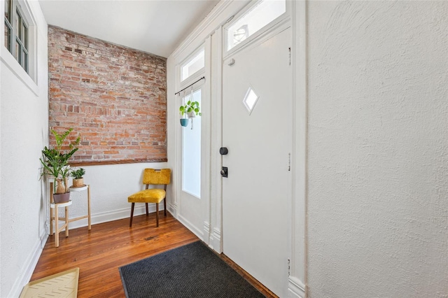 foyer entrance with baseboards, wood finished floors, brick wall, and a textured wall