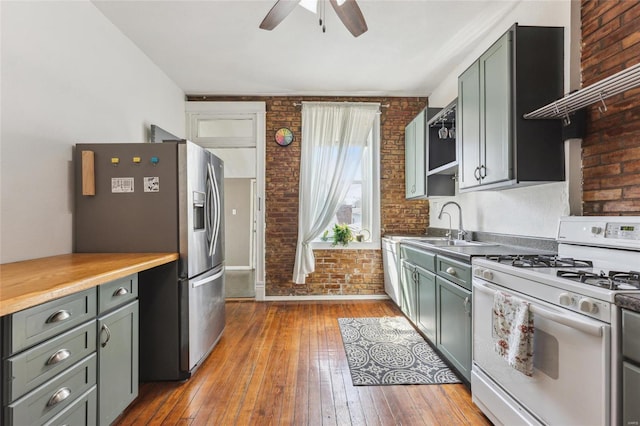 kitchen featuring ceiling fan, stainless steel fridge, white gas range, and brick wall