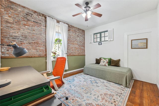 bedroom with hardwood / wood-style floors, brick wall, and ceiling fan