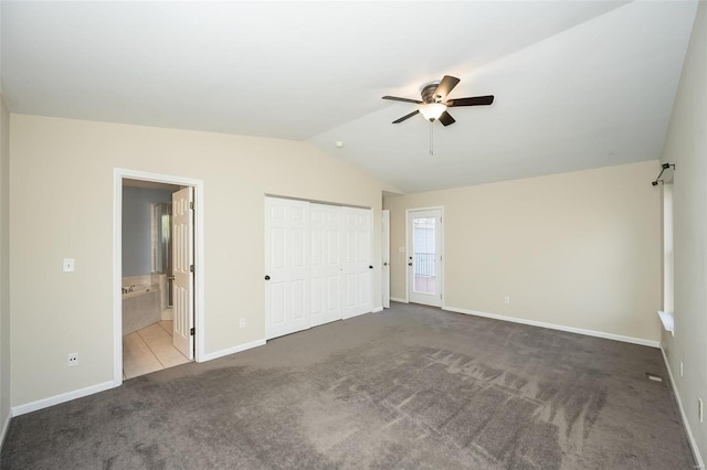 unfurnished bedroom with dark carpet, ensuite bath, ceiling fan, and vaulted ceiling