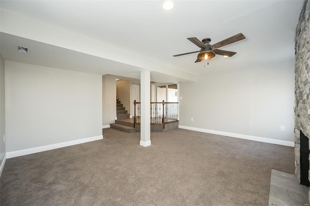 unfurnished living room featuring ceiling fan, a stone fireplace, and dark colored carpet