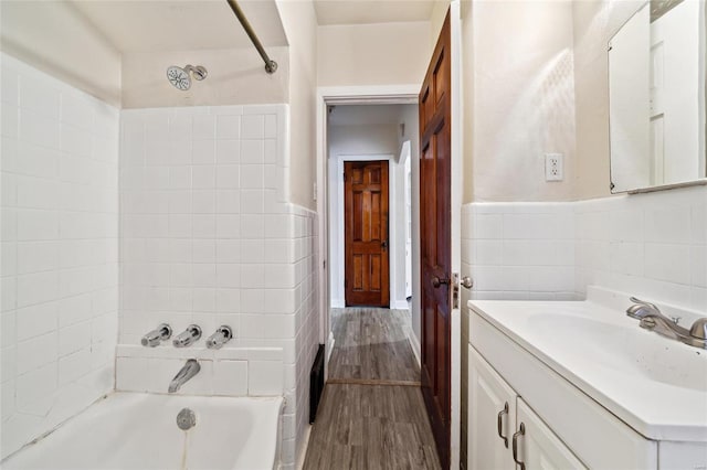 bathroom featuring vanity, hardwood / wood-style floors, tiled shower / bath combo, and tile walls