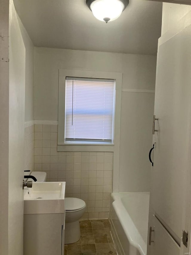 bathroom featuring tile walls, a tub to relax in, tile patterned flooring, vanity, and toilet