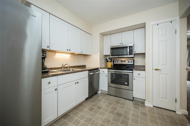 kitchen with stainless steel appliances, a sink, white cabinetry, and dark countertops