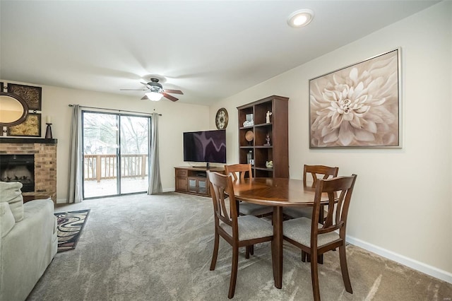 dining space with a ceiling fan, baseboards, carpet, and a brick fireplace