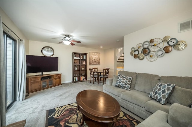 living area featuring light colored carpet, visible vents, ceiling fan, and stairs