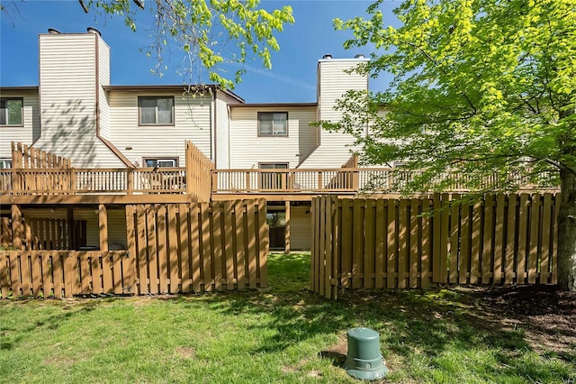 back of property with a chimney, a yard, fence, and a deck