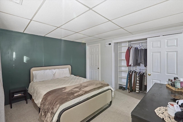 carpeted bedroom with a paneled ceiling and a closet