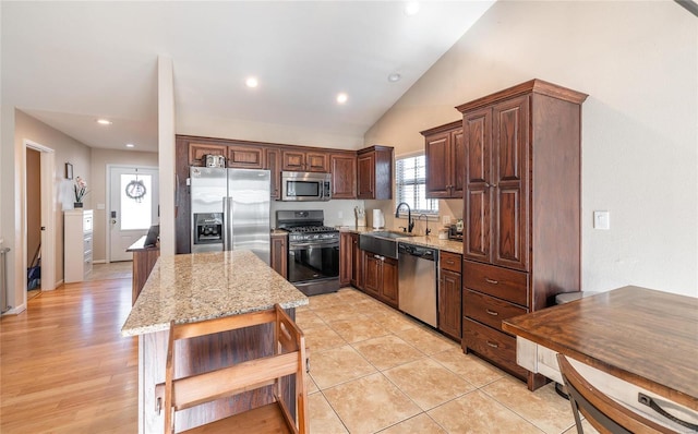 kitchen with sink, light tile patterned floors, stainless steel appliances, a center island, and light stone counters