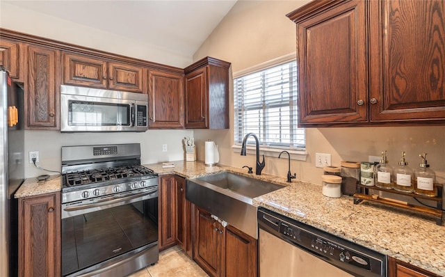 kitchen featuring lofted ceiling, sink, light stone counters, light tile patterned floors, and appliances with stainless steel finishes