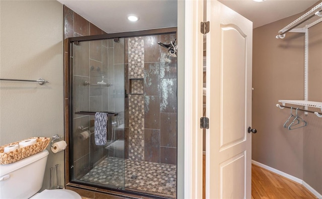 bathroom with hardwood / wood-style flooring, a shower with shower door, and toilet