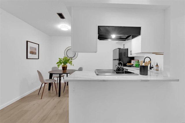 kitchen featuring light hardwood / wood-style flooring, stainless steel fridge, kitchen peninsula, white cabinets, and exhaust hood