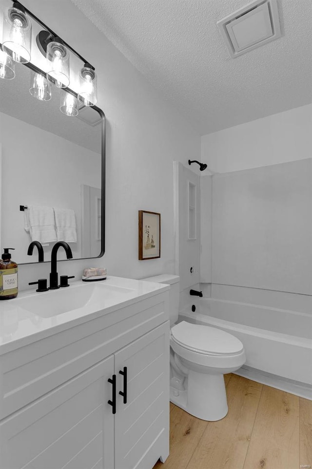 full bathroom with toilet, wood-type flooring, a textured ceiling, shower / bathtub combination, and vanity