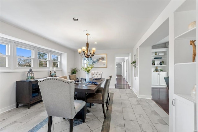 dining space with built in shelves, baseboards, and an inviting chandelier