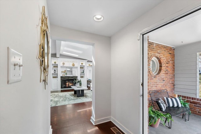 corridor featuring visible vents, built in features, dark wood-style floors, brick wall, and baseboards