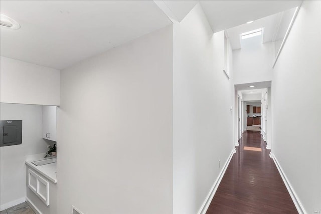 corridor featuring electric panel, wood finished floors, baseboards, and a sink