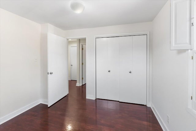 unfurnished bedroom with wood finished floors, baseboards, and a closet