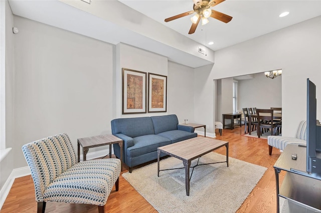 living room featuring ceiling fan with notable chandelier and light wood-type flooring