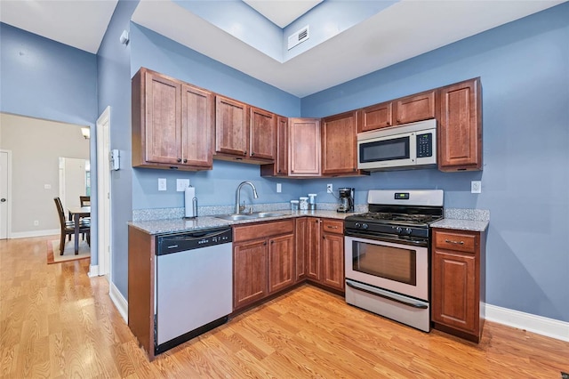 kitchen with light stone countertops, appliances with stainless steel finishes, sink, and light wood-type flooring