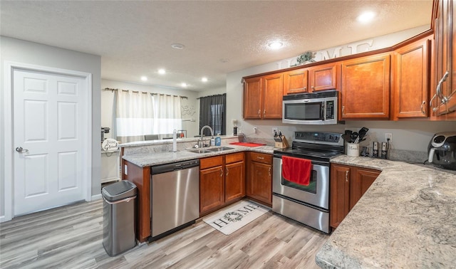 kitchen with sink, light hardwood / wood-style flooring, a textured ceiling, stainless steel appliances, and light stone countertops