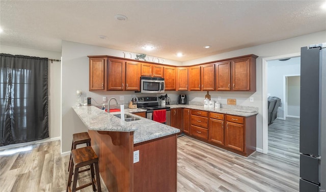 kitchen with appliances with stainless steel finishes, a breakfast bar, sink, kitchen peninsula, and light stone countertops