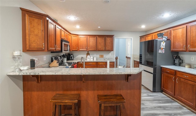 kitchen featuring appliances with stainless steel finishes, a breakfast bar, light hardwood / wood-style floors, kitchen peninsula, and light stone countertops