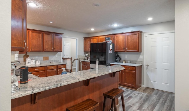 kitchen with black fridge, light stone counters, a kitchen breakfast bar, and kitchen peninsula