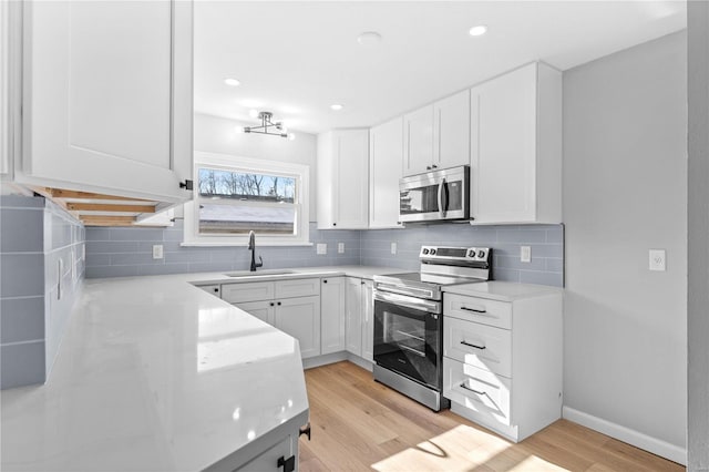 kitchen with white cabinetry, sink, stainless steel appliances, and light hardwood / wood-style floors