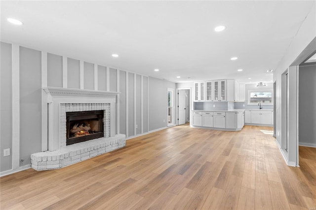 unfurnished living room with light wood-type flooring, sink, and a fireplace