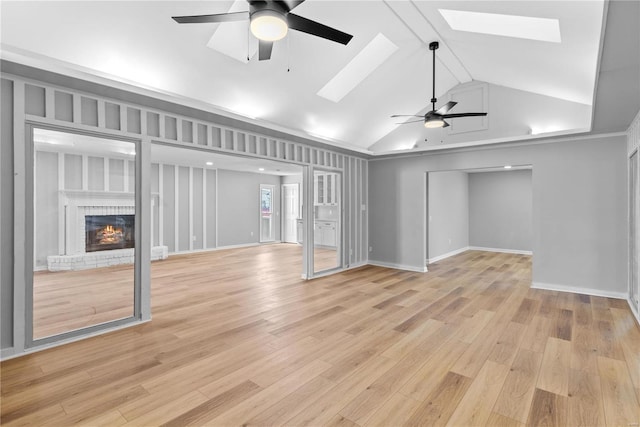 unfurnished living room featuring ceiling fan, a fireplace, a skylight, and light hardwood / wood-style flooring