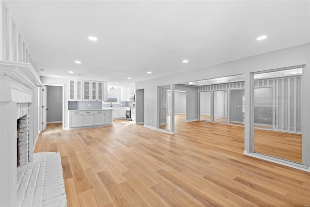 unfurnished living room with sink, a brick fireplace, and light wood-type flooring