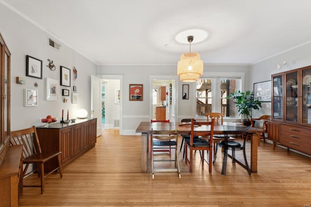 dining space with baseboards, ornamental molding, visible vents, and light wood-style floors