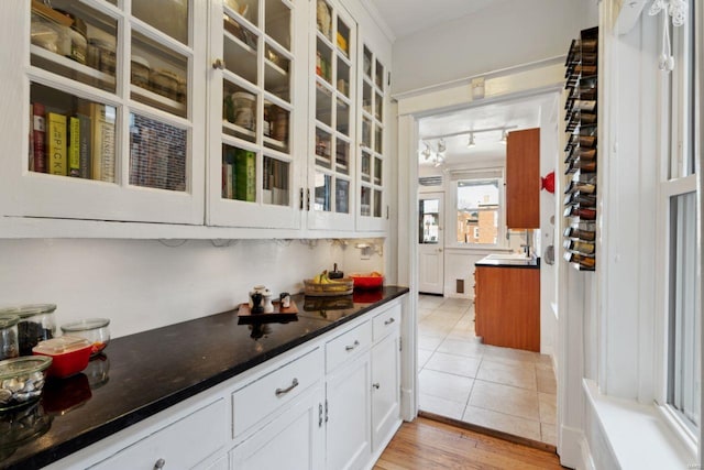 kitchen with light tile patterned floors, white cabinets, dark stone counters, glass insert cabinets, and track lighting